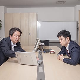 真面目な顔でパソコンをのぞき込む深田先生と弊社代表の写真